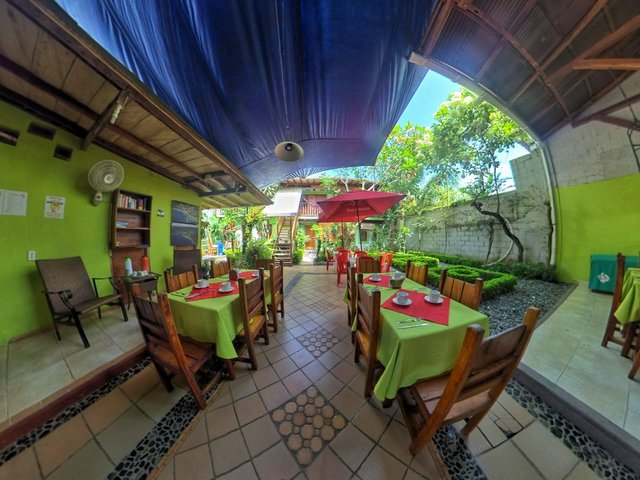 restaurante con mesas cubiertas de manteles de tela color verde manzana, con sobremanteles rojos, sillas de madera en un jardin abierto con carpa de lona color azul
